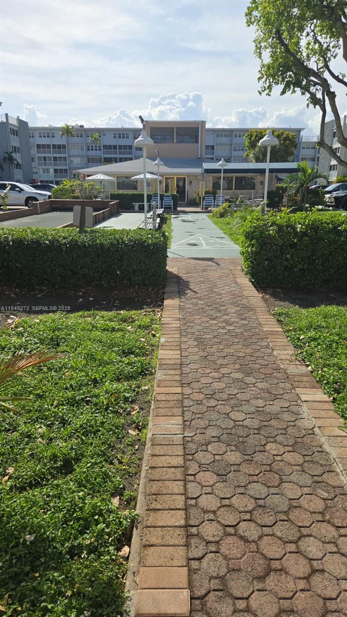 A brick walkway leads toward a community building with shuffleboard courts and outdoor seating — 215 SE 3rd Ave # 403A, Hallandale Beach FL 33009, HALLANDALE BEACH, FL