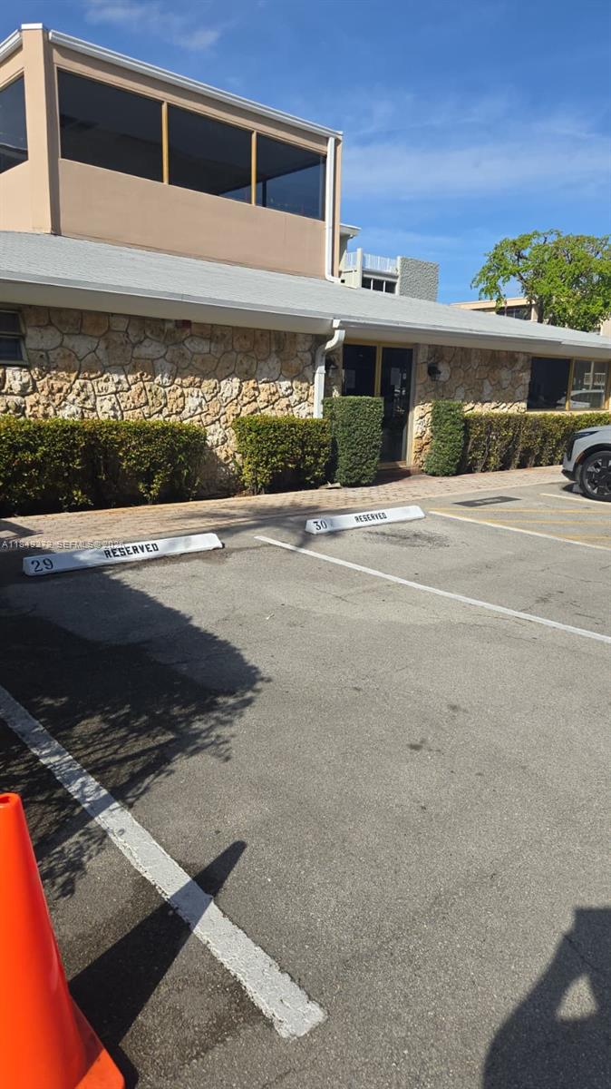 A low-rise building with a stone facade features reserved parking spaces in the foreground — 215 SE 3rd Ave # 403A, Hallandale Beach FL 33009, HALLANDALE BEACH, FL