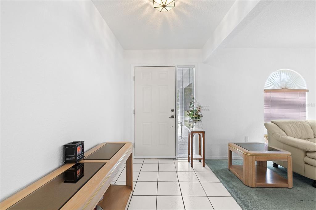A bright entryway features white tiled floors, a white front door, and a wooden console table — 3923 PINSTAR TER, NORTH PORT, FL