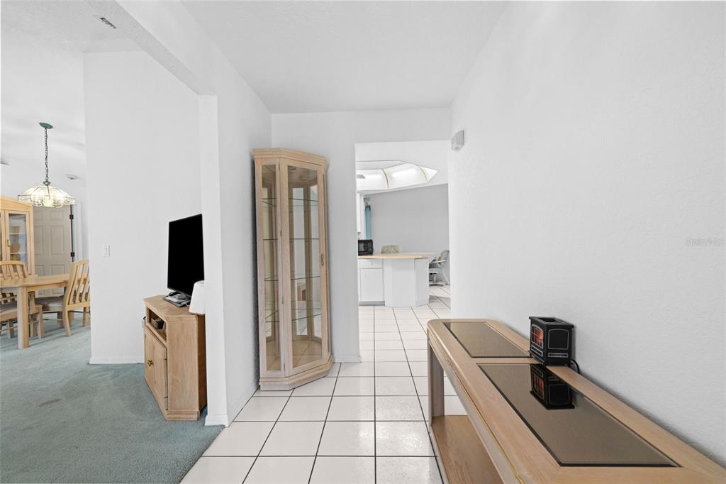 A hallway with white tile flooring connects a carpeted dining area to a kitchen — 3923 PINSTAR TER, NORTH PORT, FL