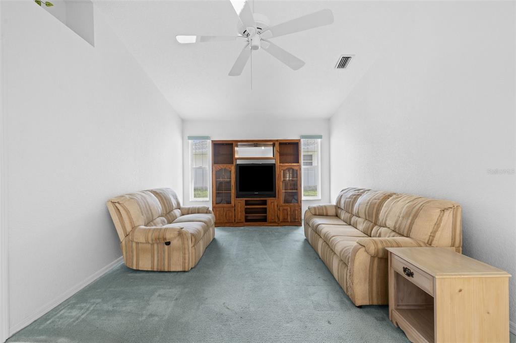 A living room features two striped sofas, a wooden entertainment center, and blue carpeting — 3923 PINSTAR TER, NORTH PORT, FL