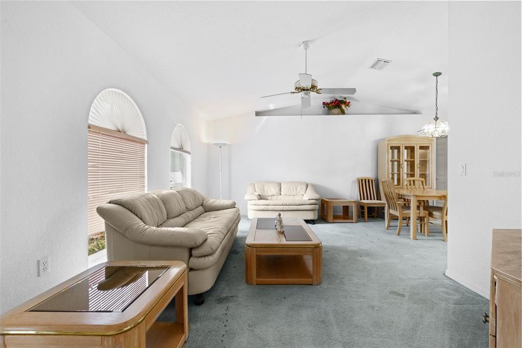 A living room with a beige sofa, coffee table, and dining area on blue carpet — 3923 PINSTAR TER, NORTH PORT, FL