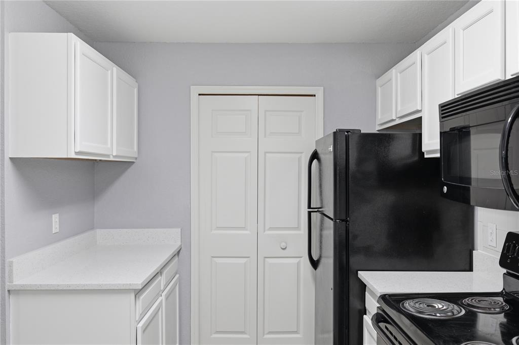 A kitchen features white cabinets, light countertops, and black appliances against light gray walls — 7605 PISSARRO DRIVE UNIT 13204, ORLANDO, FL