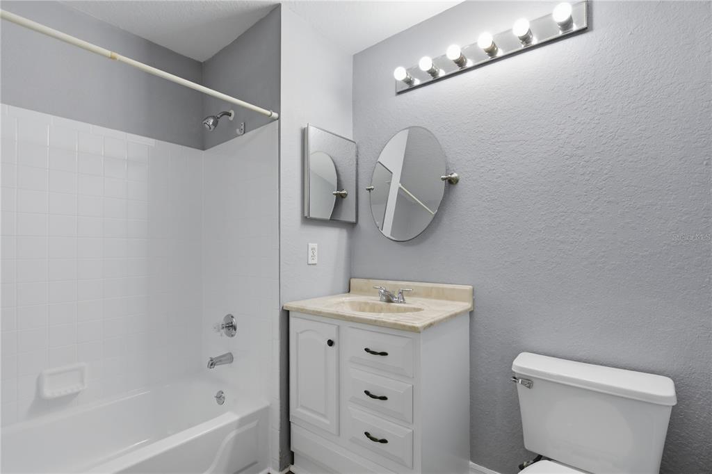 A bathroom features a white vanity, a round mirror, a toilet, and a shower-tub combo — 7605 PISSARRO DRIVE UNIT 13204, ORLANDO, FL