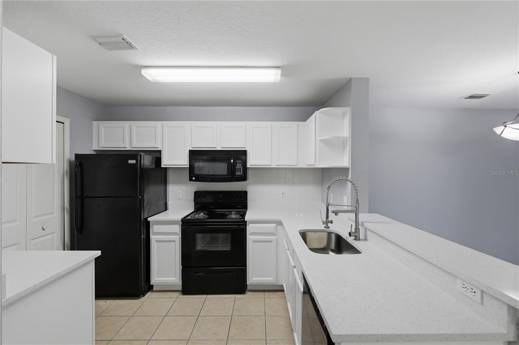 A kitchen features white cabinets, black appliances, a breakfast bar, and light-colored countertops — 7605 PISSARRO DRIVE UNIT 13204, ORLANDO, FL