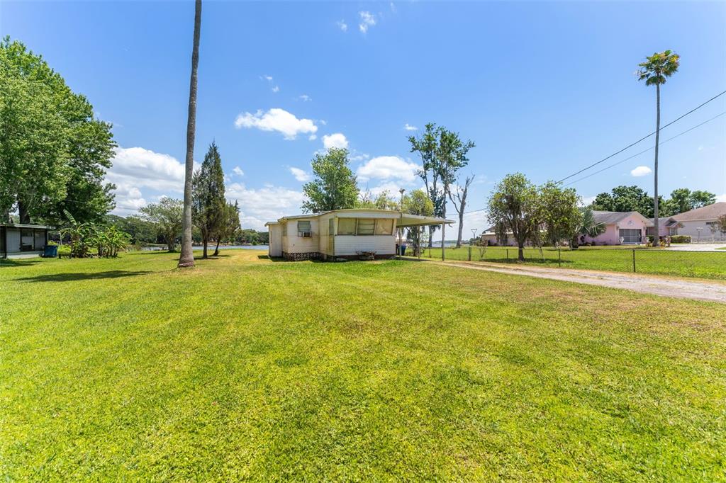 A single-story mobile home sits on a large, grassy lot near a body of water — 7558 BERKLEY ROAD, POLK CITY, FL