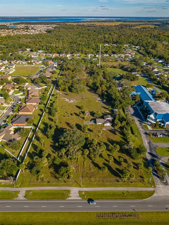 An aerial view shows a large, grassy vacant lot situated between a residential neighborhood and commercial buildings — 4051 PLEASANT HILL ROAD, KISSIMMEE, FL