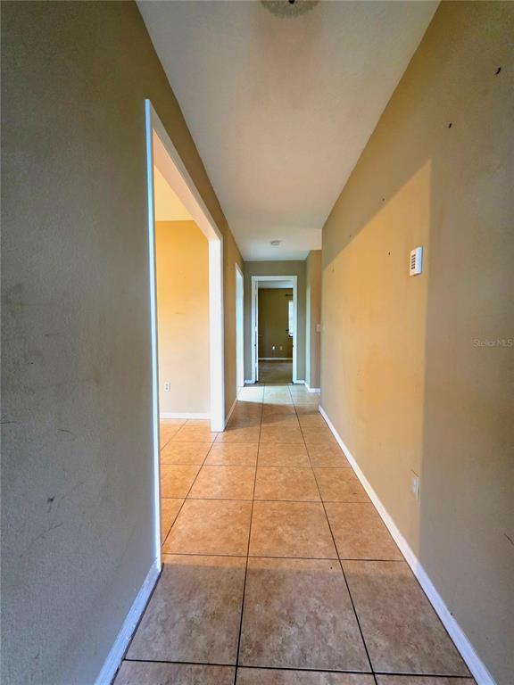 A hallway with tan walls and light-colored square floor tiles leads to another room — 125 OAK CIRCLE, OCALA, FL