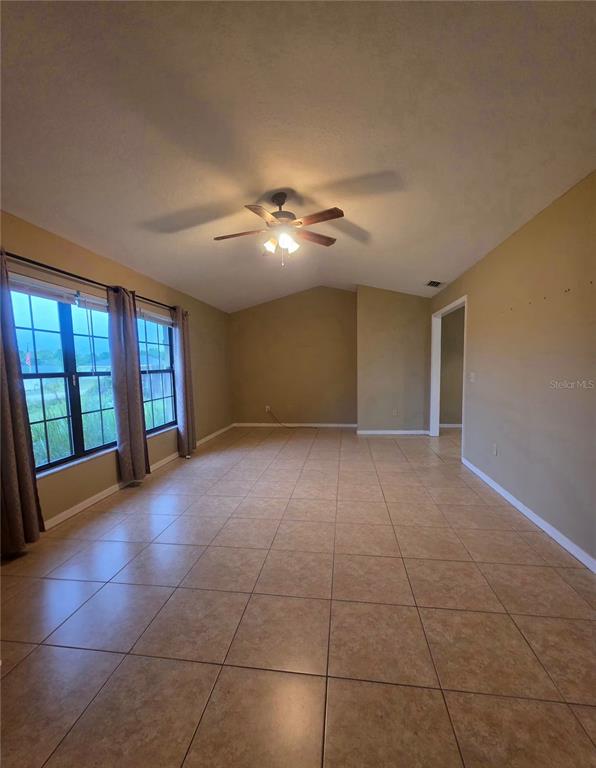 A spacious living room features tan tile flooring, a vaulted ceiling, and a ceiling fan — 125 OAK CIRCLE, OCALA, FL