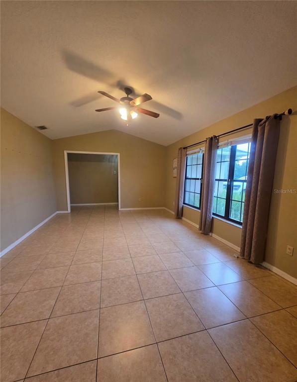 A living room features tan tile flooring, a vaulted ceiling with a fan, and large windows — 125 OAK CIRCLE, OCALA, FL