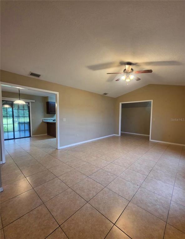 A spacious living area with tan tile floors, a ceiling fan, and two arched doorways — 125 OAK CIRCLE, OCALA, FL