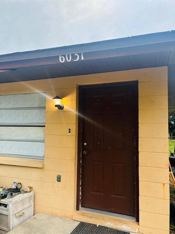 The exterior of a house features a brown door, a wall-mounted lamp, and house number 6031 — 6031 CRAFTON DRIVE, LAKELAND, FL