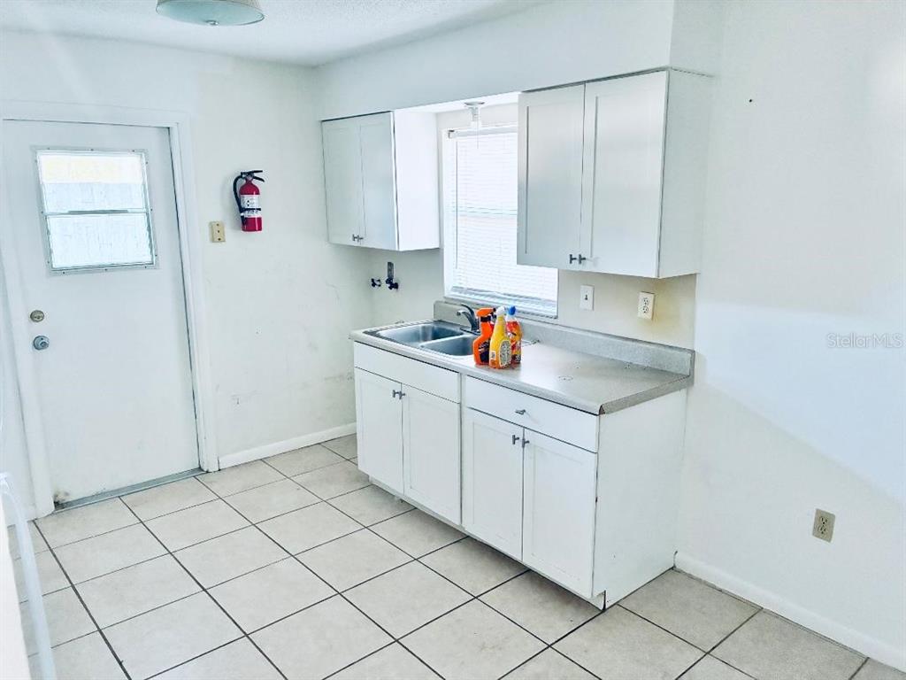 A kitchen features white cabinets, a stainless steel sink, and light-colored tile flooring — 6031 CRAFTON DRIVE, LAKELAND, FL
