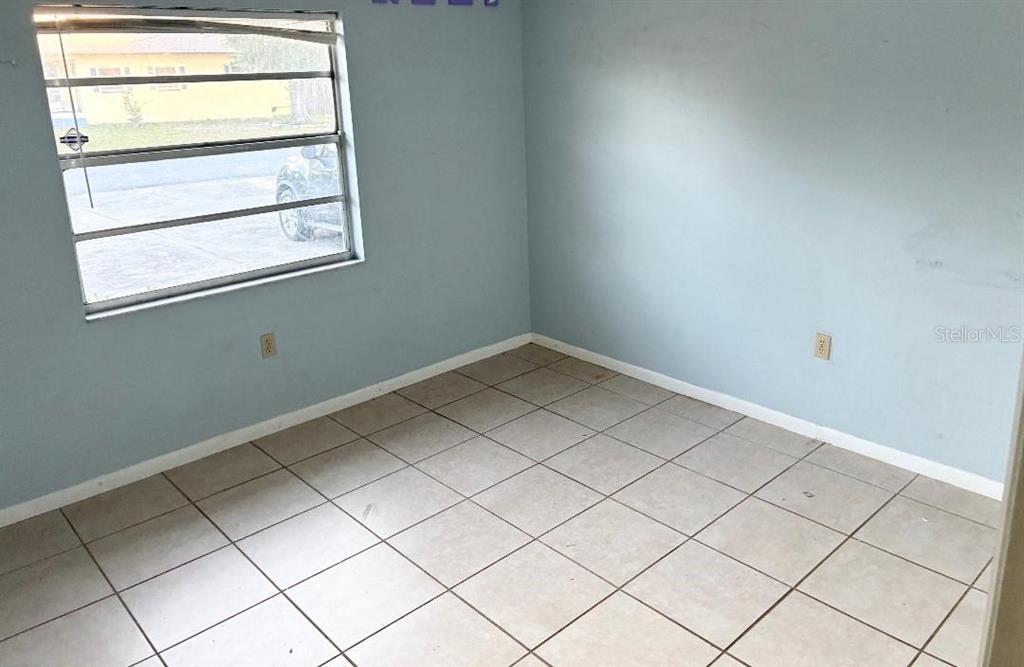 An empty room with light blue walls and beige tiled flooring features a single window — 6031 CRAFTON DRIVE, LAKELAND, FL