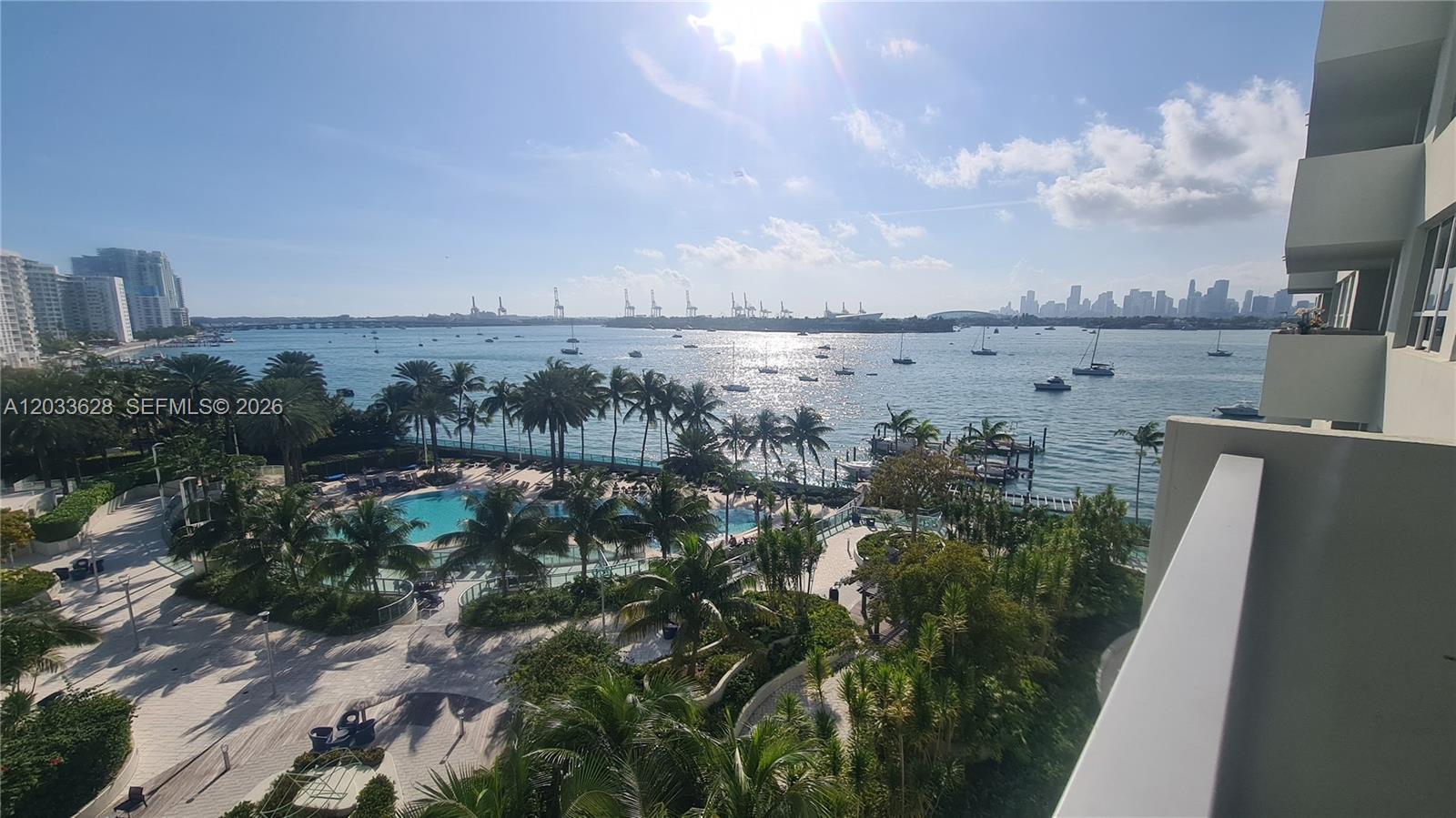 A high-angle view shows a swimming pool, palm trees, and a bay with boats — MIAMI BEACH, FL