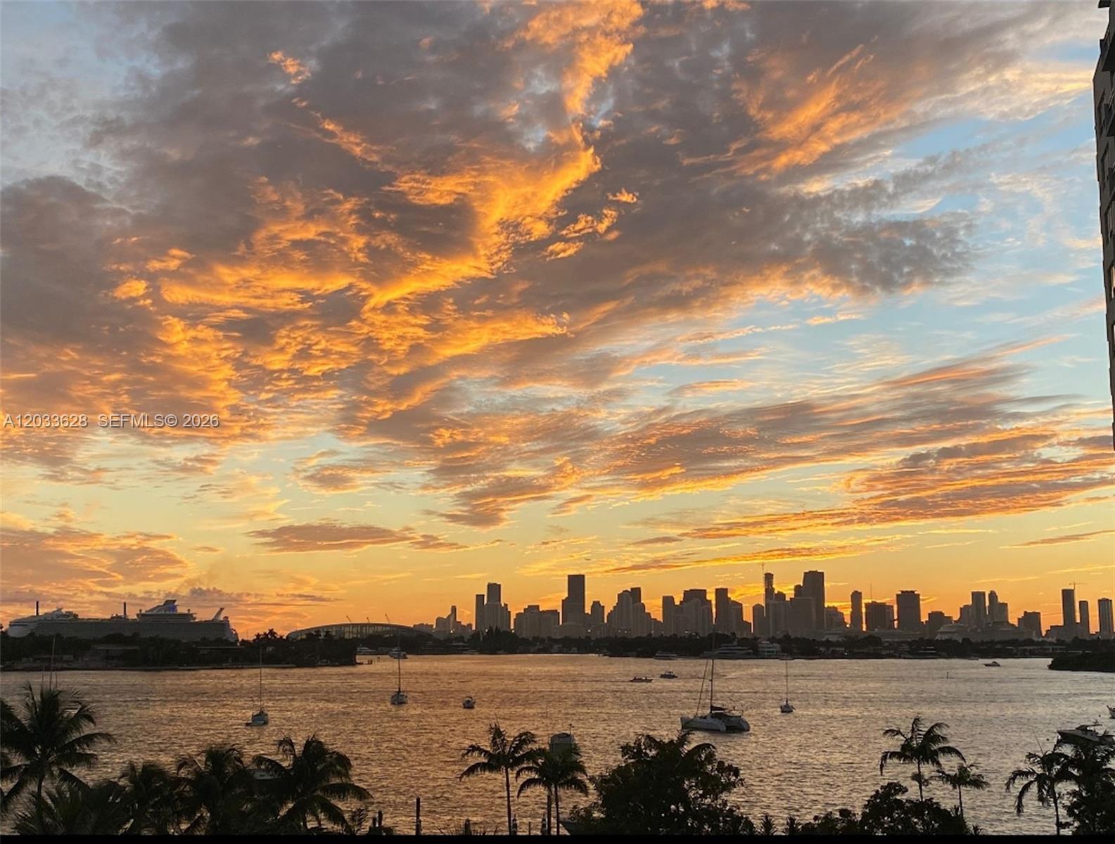 A sunset view over the Miami skyline and bay with boats in the water — MIAMI BEACH, FL
