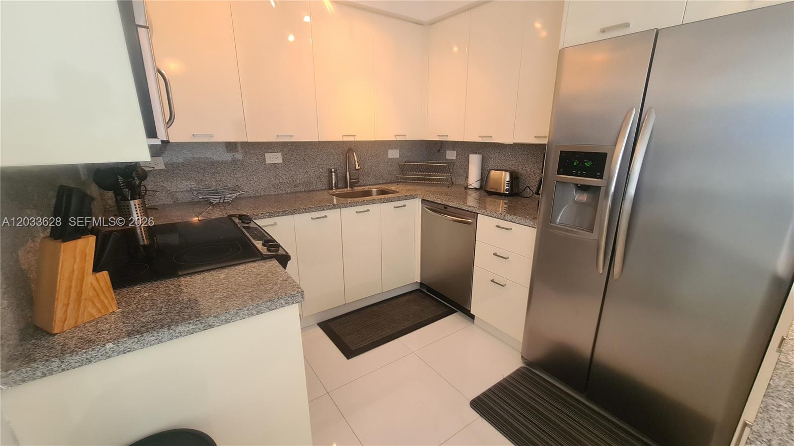 A kitchen features white cabinets, granite countertops, stainless steel appliances, and white tile flooring — MIAMI BEACH, FL
