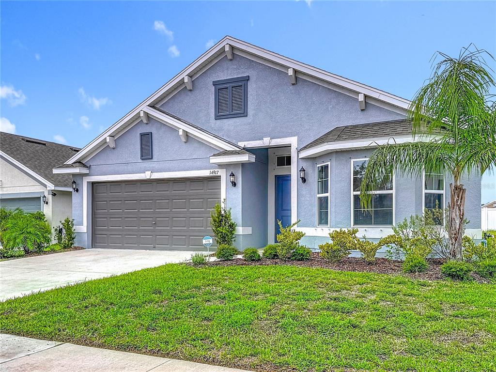 A blue single-story house features a two-car garage, a front entrance, and a palm tree — 14917 TROPICAL VIOLET WAY, WIMAUMA, FL