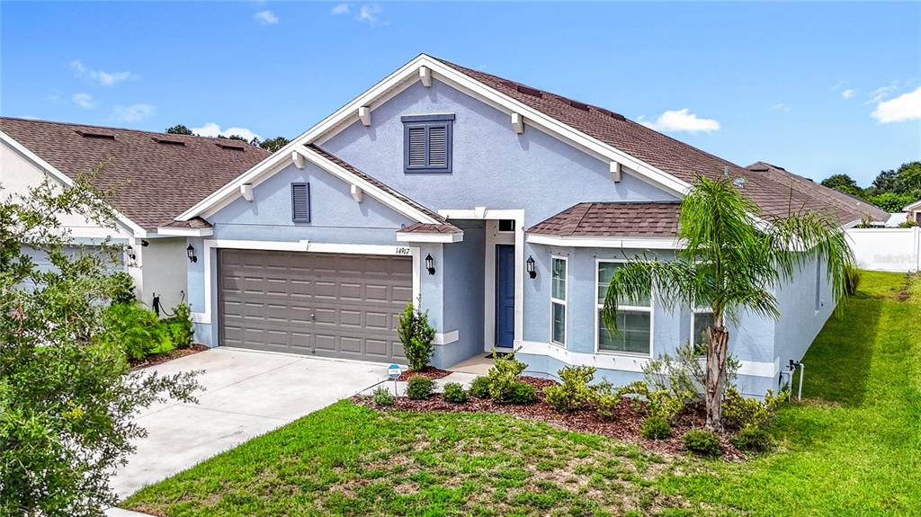 A blue single-story house with a two-car garage, brown roof, and a front lawn — 14917 TROPICAL VIOLET WAY, WIMAUMA, FL