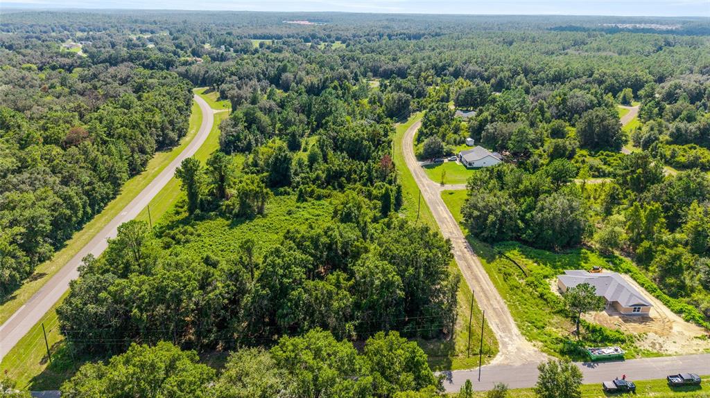 An aerial view shows a wooded lot situated between two paved roads with nearby houses — 714 E IRENE LANE, CITRUS SPRINGS, FL