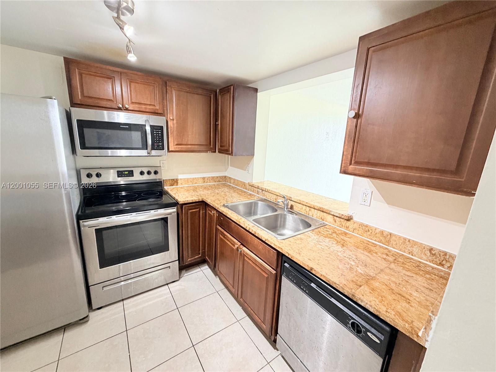 A kitchen features stainless steel appliances, wood cabinets, and tan granite countertops — 496 NW 165th St Rd # 409, Miami FL 33169, MIAMI, FL