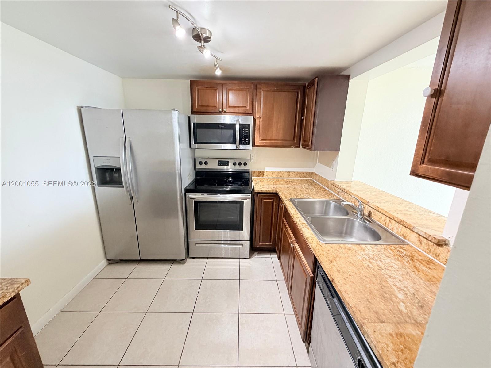 A kitchen features stainless steel appliances, wood cabinets, and granite countertops over tile flooring — 496 NW 165th St Rd # 409, Miami FL 33169, MIAMI, FL