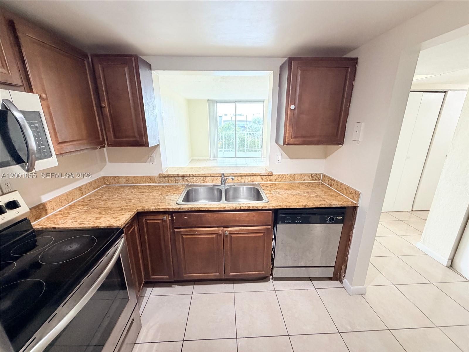 A kitchen features wood cabinets, granite countertops, stainless steel appliances, and a pass-through window — 496 NW 165th St Rd # 409, Miami FL 33169, MIAMI, FL