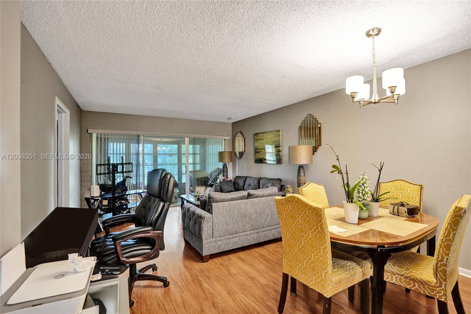 A living and dining area features wood-look flooring, a gray sofa, and yellow patterned chairs — 5961 NW 61st Ave # 310, Tamarac FL 33319, TAMARAC, FL