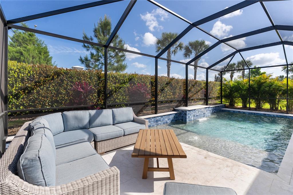 A covered patio features a dining set, lounge furniture, and a pool with a waterfall — 17526 SAVORY MIST CIRCLE, BRADENTON, FL