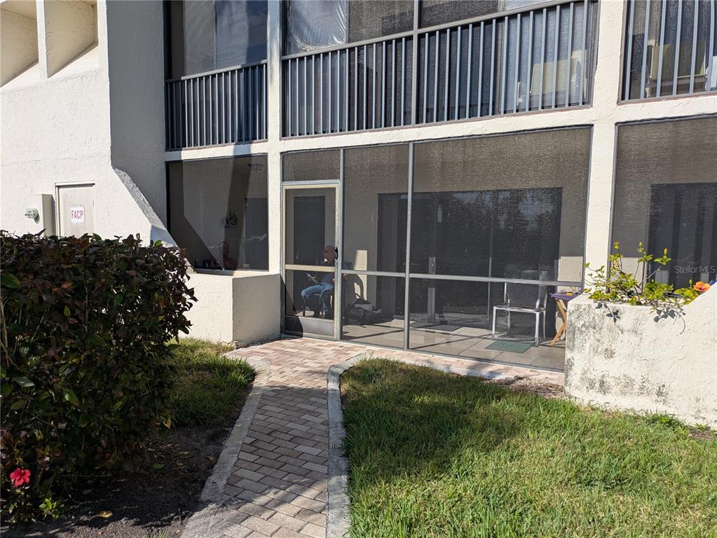 A ground-level patio with a screen enclosure and a brick walkway leading to the door — 6114 43RD STREET W UNIT 106E, BRADENTON, FL