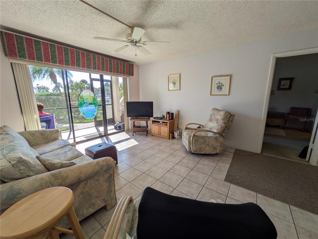 A living room features tile flooring, a ceiling fan, floral furniture, and a sliding glass door — 6114 43RD STREET W UNIT 106E, BRADENTON, FL