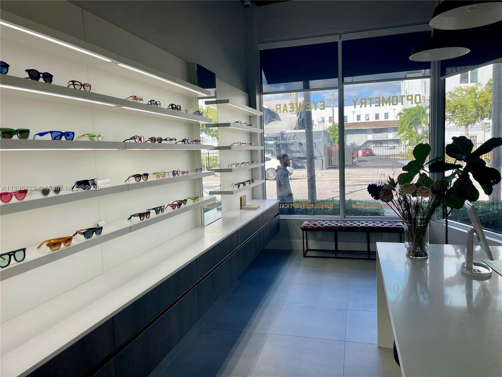 An optometry office features illuminated wall shelving displaying eyeglasses, a white counter, and a window — 536 SW 12th Ave, Miami FL 33130, MIAMI, FL