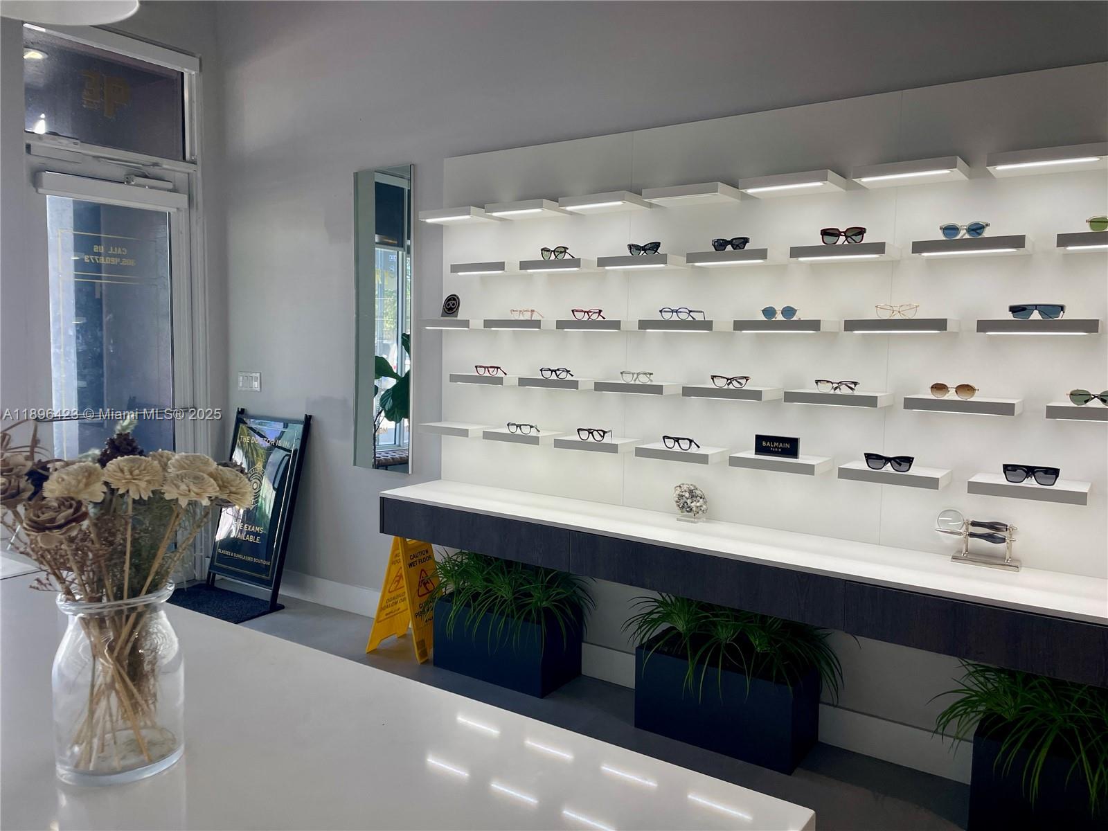A modern optical store features illuminated wall-mounted shelves displaying eyeglasses above dark planters — 536 SW 12th Ave, Miami FL 33130, MIAMI, FL
