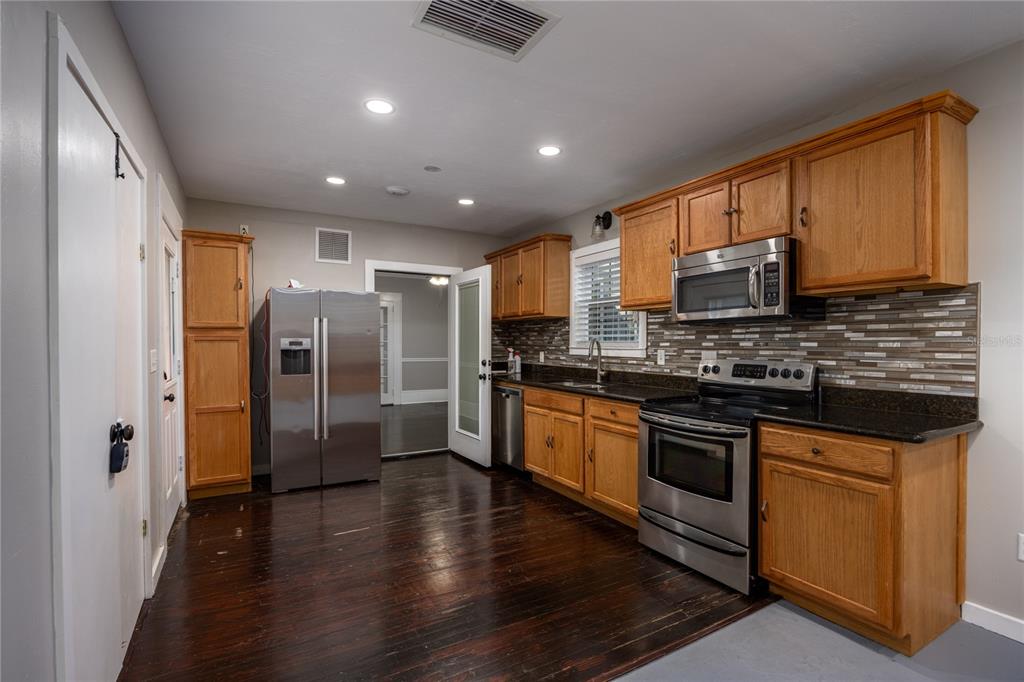 A kitchen with wood cabinets, stainless steel appliances, dark countertops, and dark wood flooring — 18420 HIGH SPRINGS MAIN STREET, HIGH SPRINGS, FL