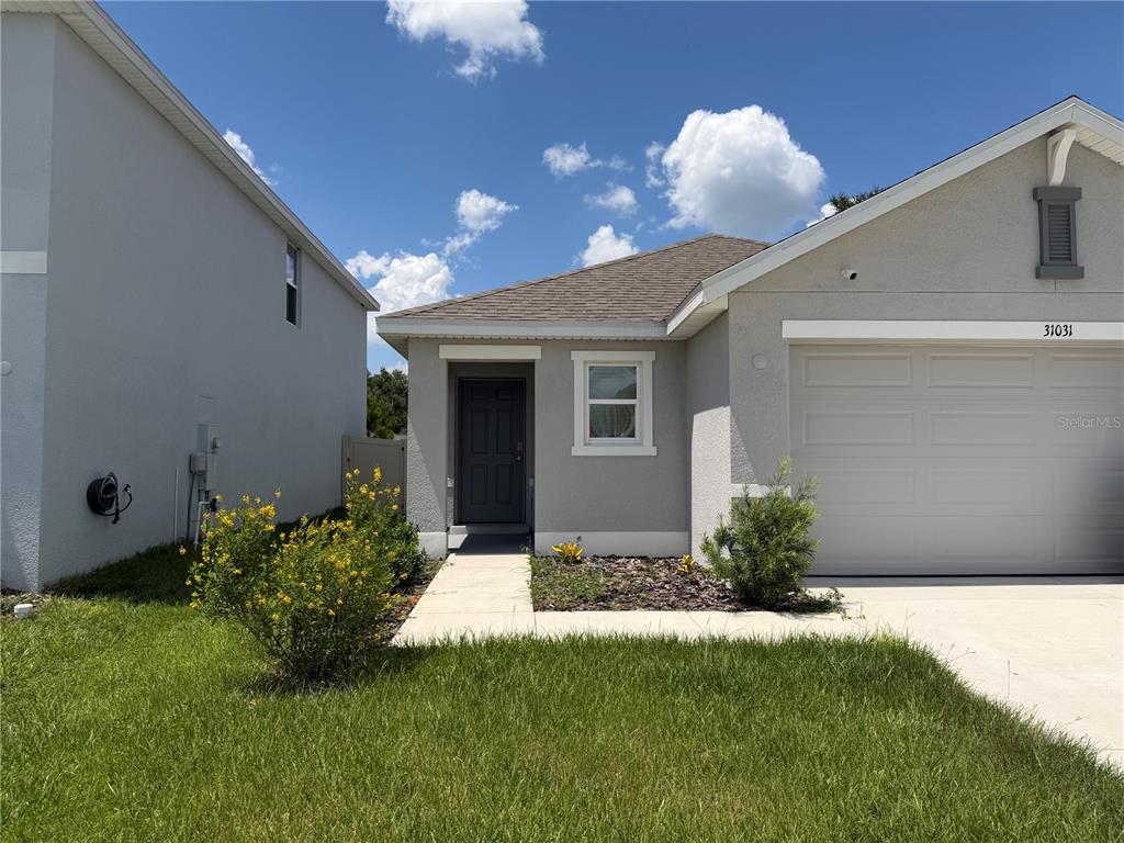 A single-story house features a gray exterior, a front-facing garage, and a small landscaped yard — 31031 SILVER STAGE DRIVE, BROOKSVILLE, FL