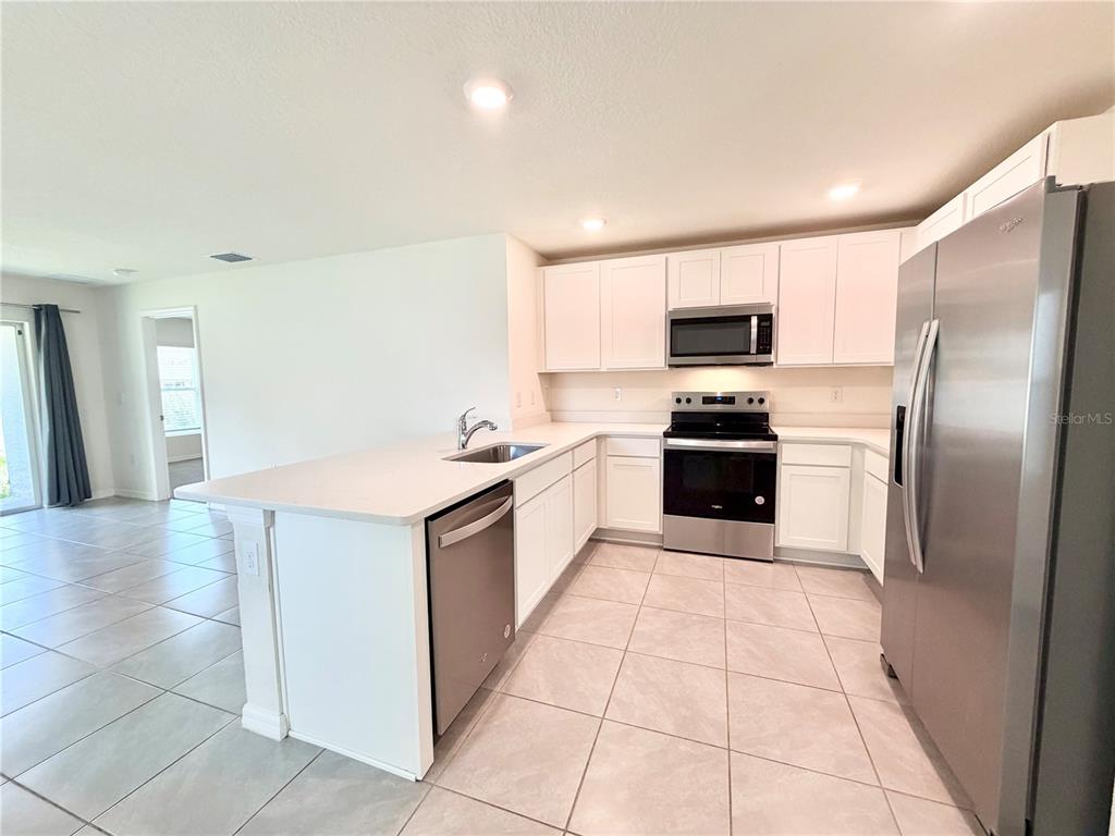 A kitchen features white cabinets, stainless steel appliances, and light tile flooring — 31031 SILVER STAGE DRIVE, BROOKSVILLE, FL