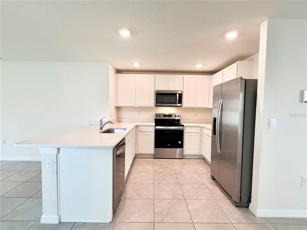A kitchen features white cabinets, stainless steel appliances, a kitchen island, and tiled flooring — 31031 SILVER STAGE DRIVE, BROOKSVILLE, FL