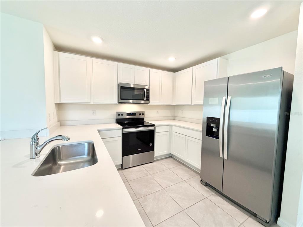 A modern kitchen features white cabinets, stainless steel appliances, and light-colored countertops — 31031 SILVER STAGE DRIVE, BROOKSVILLE, FL