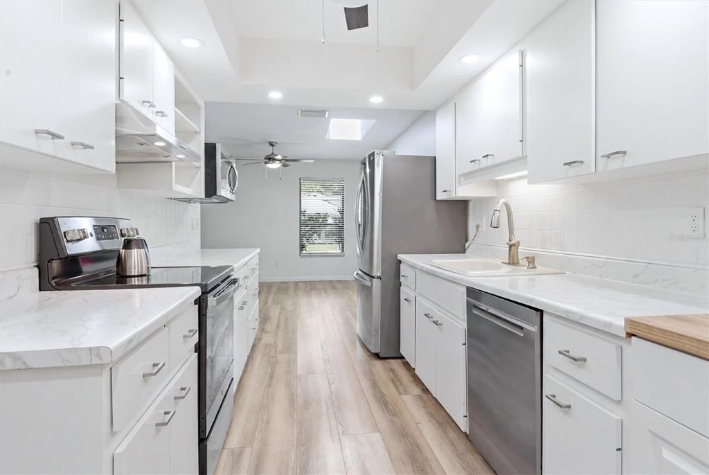 A galley kitchen features white cabinets, stainless steel appliances, and light wood-look flooring — 4793 OAK FOREST DRIVE W UNIT 46, SARASOTA, FL