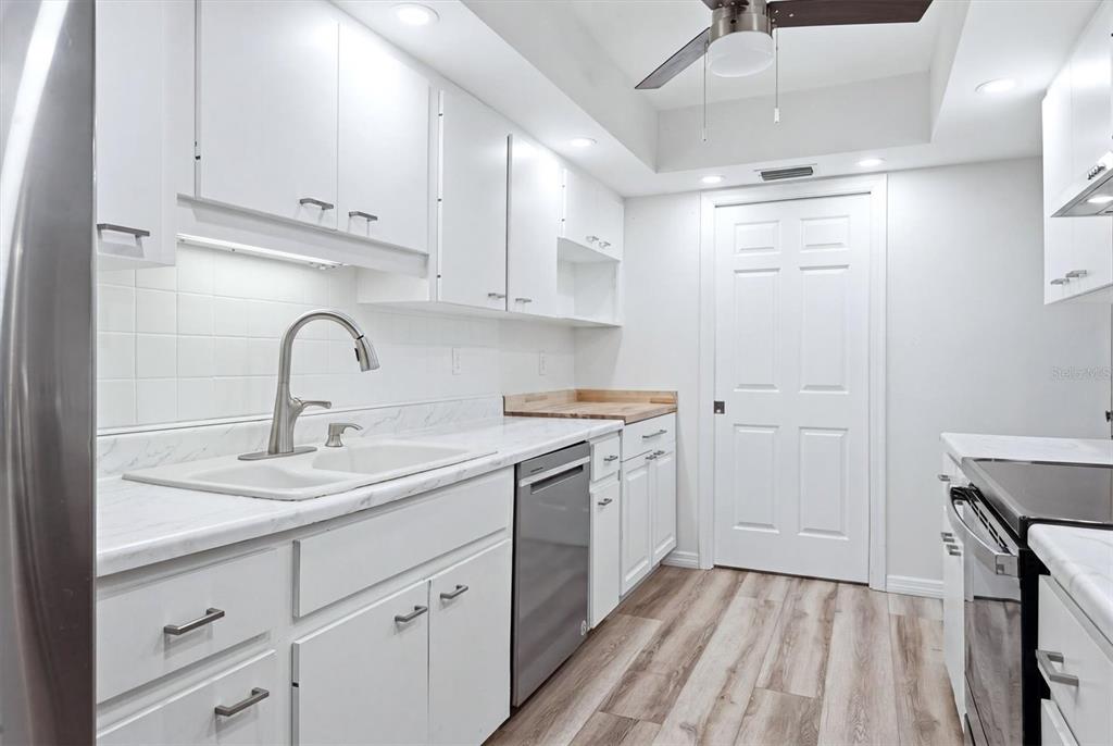 A white kitchen features light wood-look flooring, stainless steel appliances, and white cabinetry — 4793 OAK FOREST DRIVE W UNIT 46, SARASOTA, FL