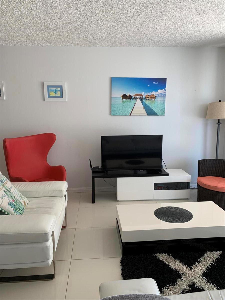 A living room features a white sofa, red accent chair, television console, and coffee table — 101 Briny Avenue # 806, Pompano Beach FL 33062, POMPANO BEACH, FL