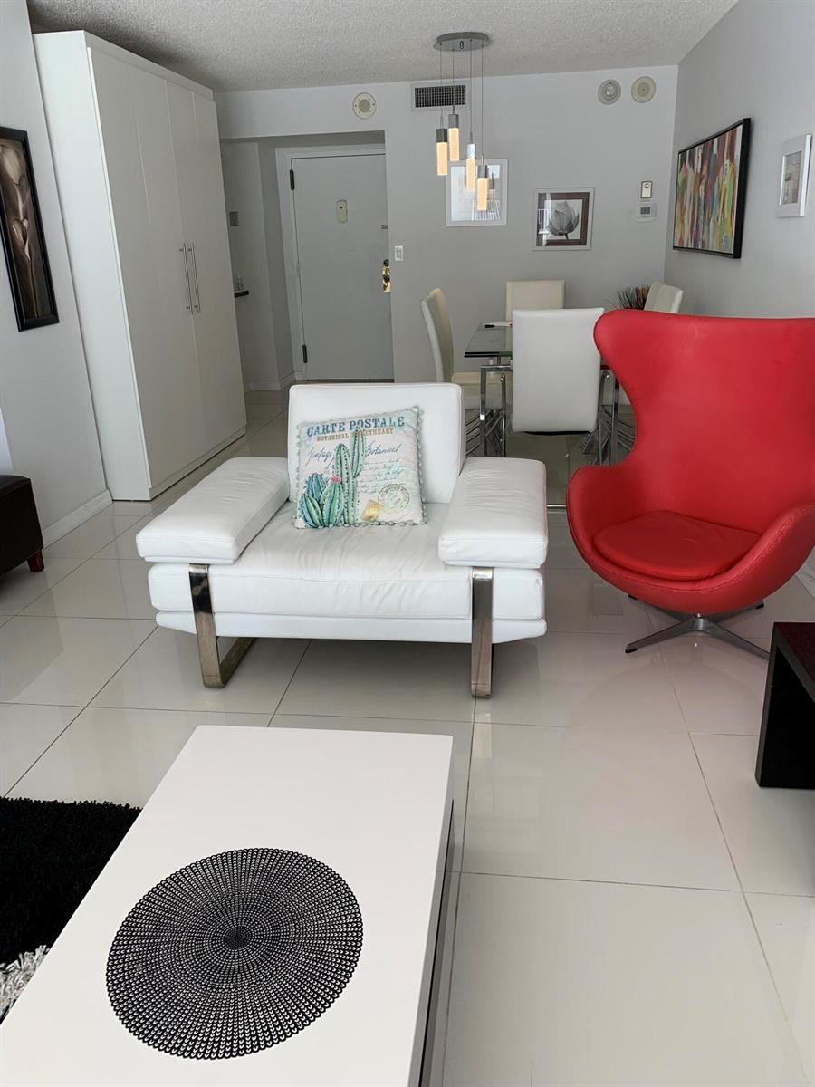 A modern living and dining area features white tile floors, a white armchair, and red chair — 101 Briny Avenue # 806, Pompano Beach FL 33062, POMPANO BEACH, FL