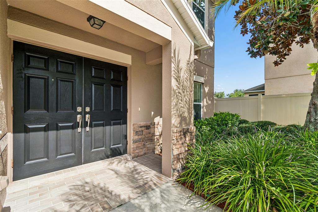 A front entryway features double black doors, a brick porch, and stone accents on the exterior — 9615 REGIMENT COURT, LAND O LAKES, FL