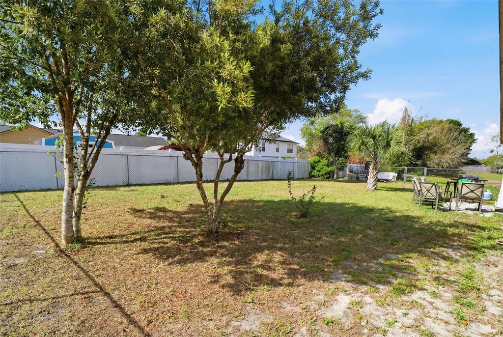 A grassy backyard features two prominent trees, a white chain-link fence, and patio furniture — 783 S ATMORE CIRCLE, DELTONA, FL