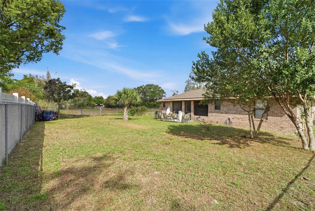 A grassy backyard features a brick house, a patio area, and a chain-link fence — 783 S ATMORE CIRCLE, DELTONA, FL