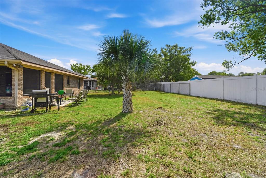 A backyard features a palm tree, a brick house with a patio, and a white fence — 783 S ATMORE CIRCLE, DELTONA, FL