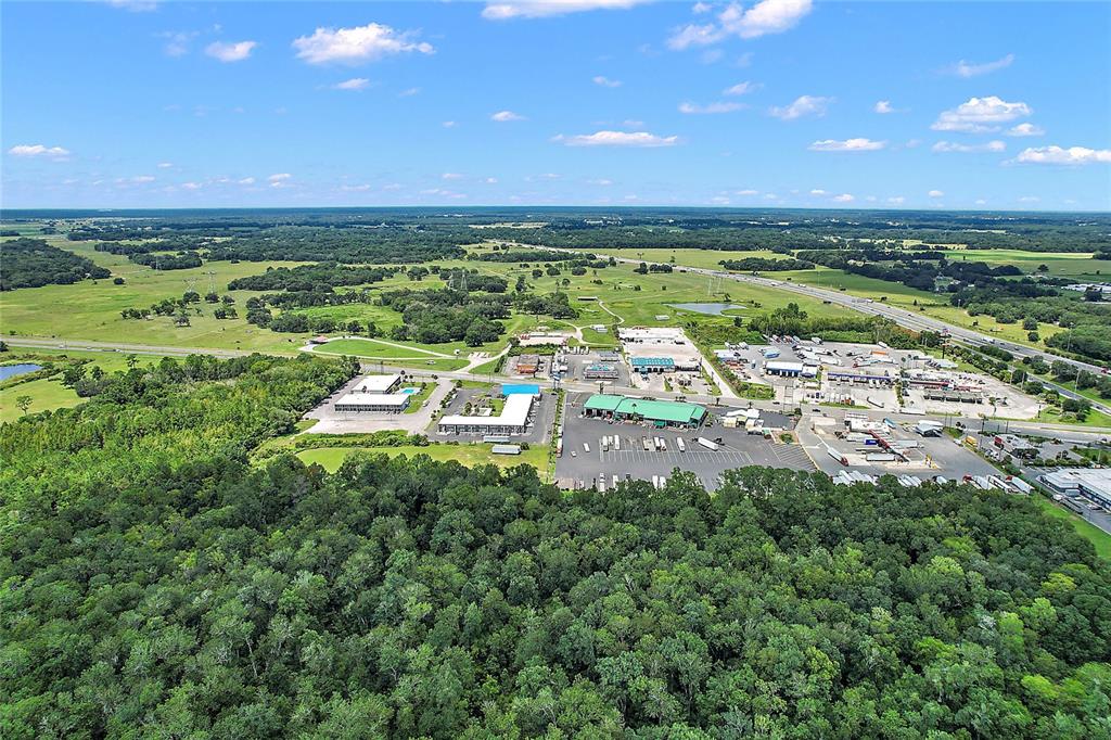 An aerial view shows a commercial area with parking lots and buildings surrounded by dense forest — 412 E STATE ROAD 44, WILDWOOD, FL