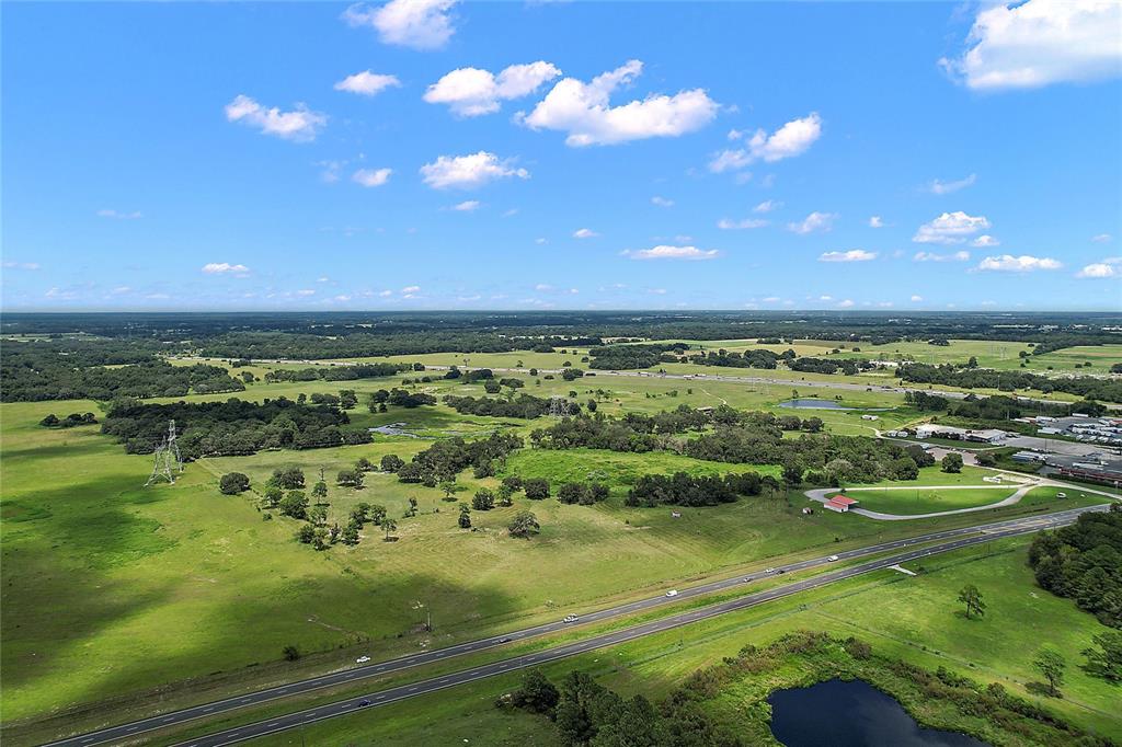 An aerial view shows a large, grassy rural landscape with a highway and a pond — 412 E STATE ROAD 44, WILDWOOD, FL