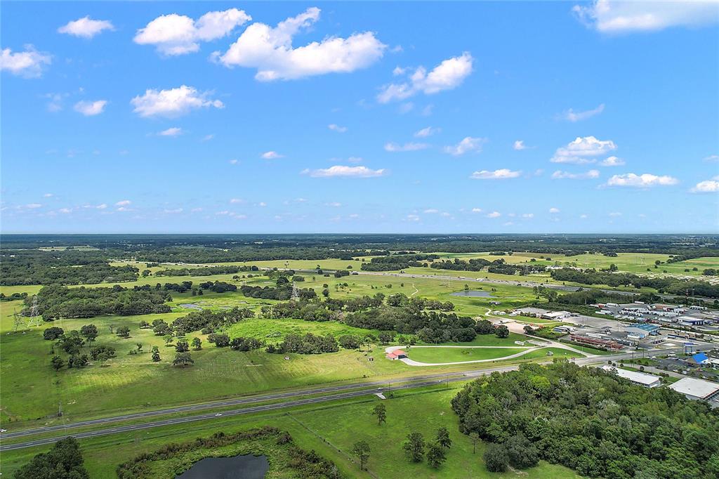 An aerial view shows a rural landscape with a highway, green fields, and scattered trees — 412 E STATE ROAD 44, WILDWOOD, FL