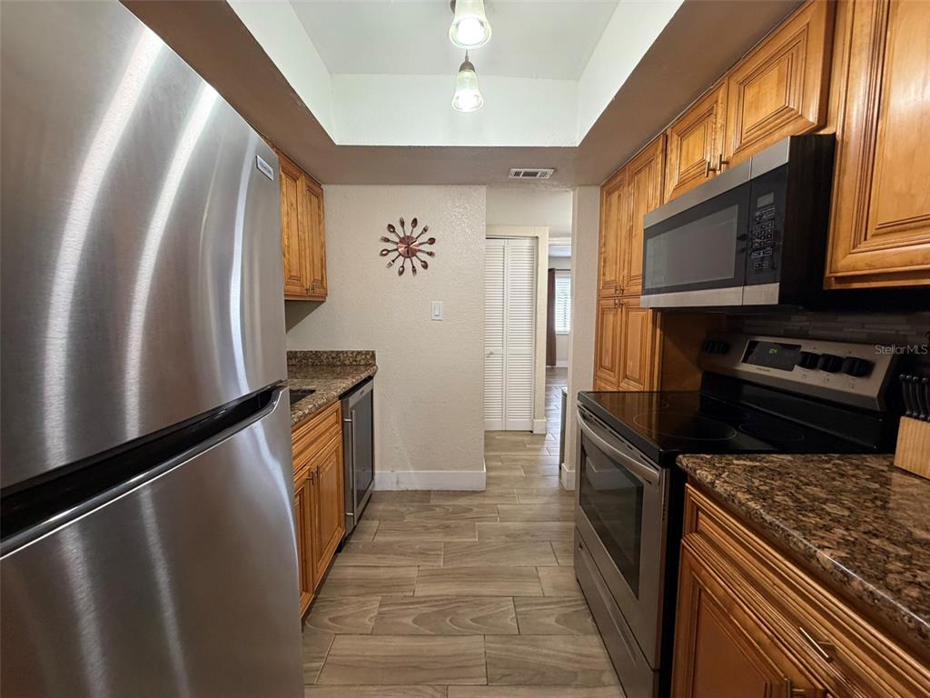 A galley kitchen features stainless steel appliances, wood cabinets, granite countertops, and light-colored tile flooring — 4807 S TEXAS AVENUE UNIT 4807C, ORLANDO, FL